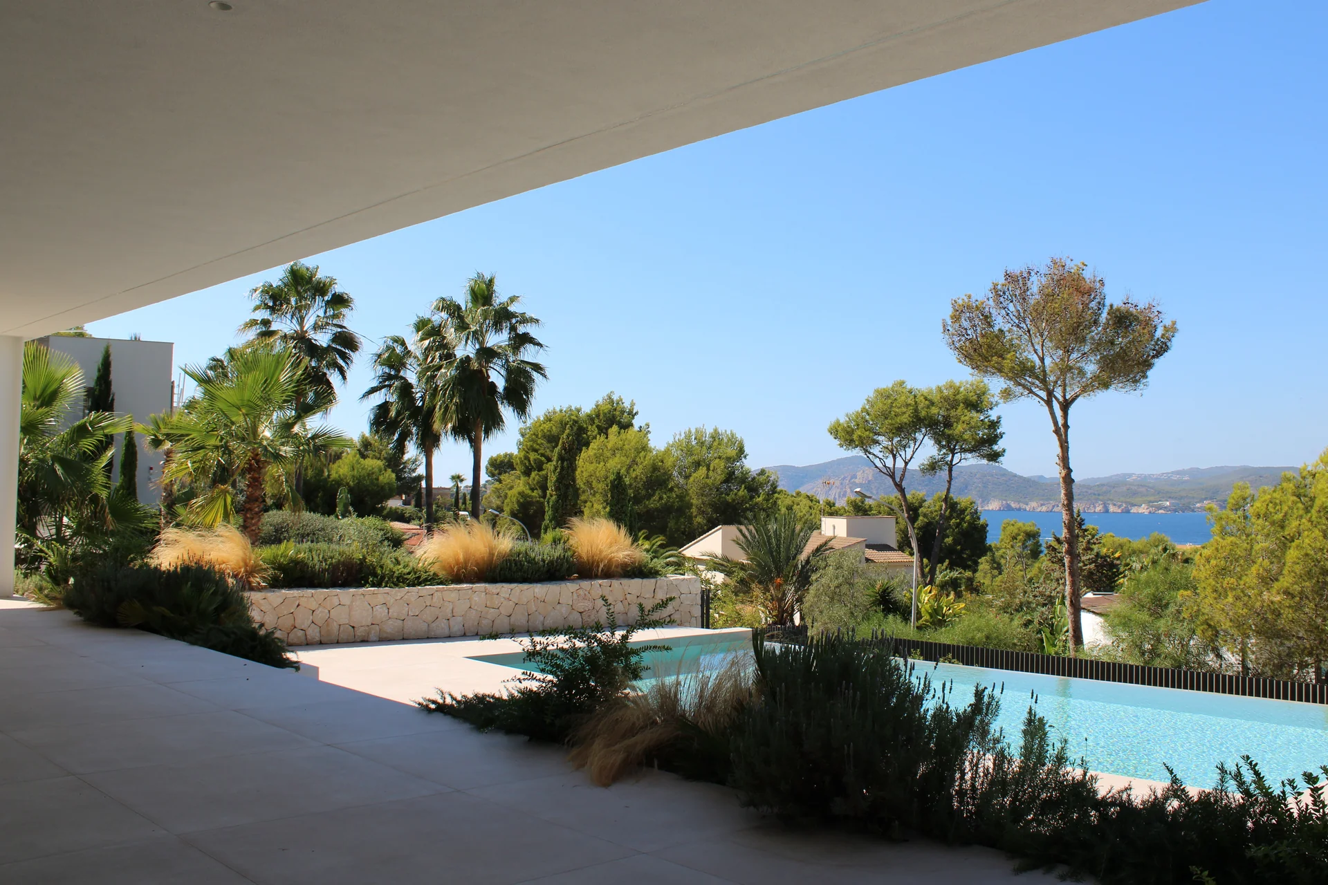 Porche cubierto con vistas a la piscina infinita, vegetación mediterránea y la costa de Calvià - S'Estepa Design